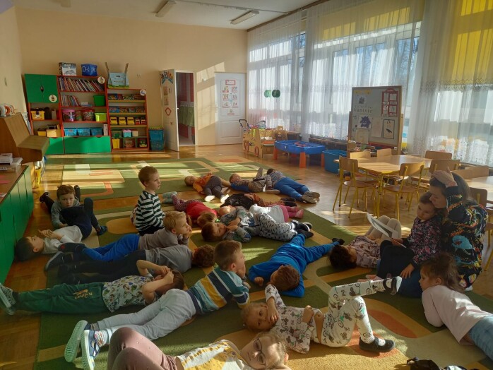 Dzieci leżą na dywanie, prowadząca czyta bajkę.