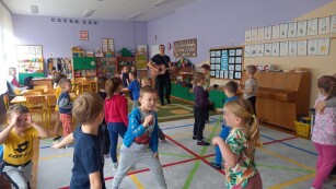 Prowadzący gra na gitarze, dzieci tańczą.